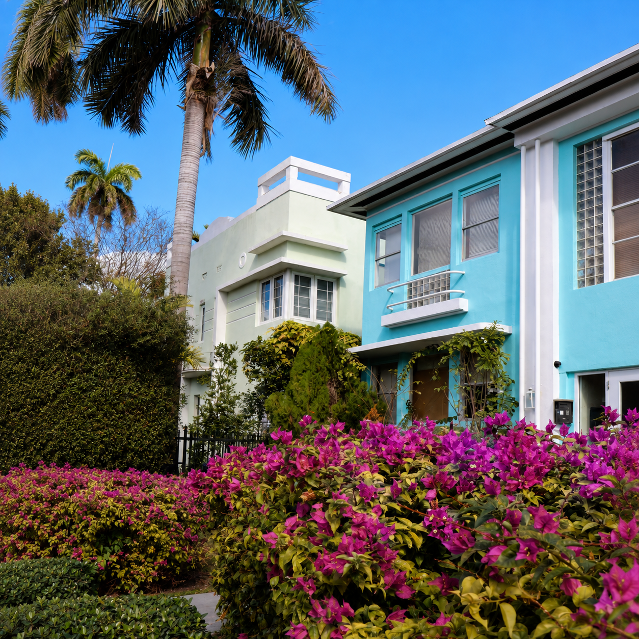 Blue Stone home next to a white stone home against blue sky with palm trees in Century Gardens, Hialeah, fl
