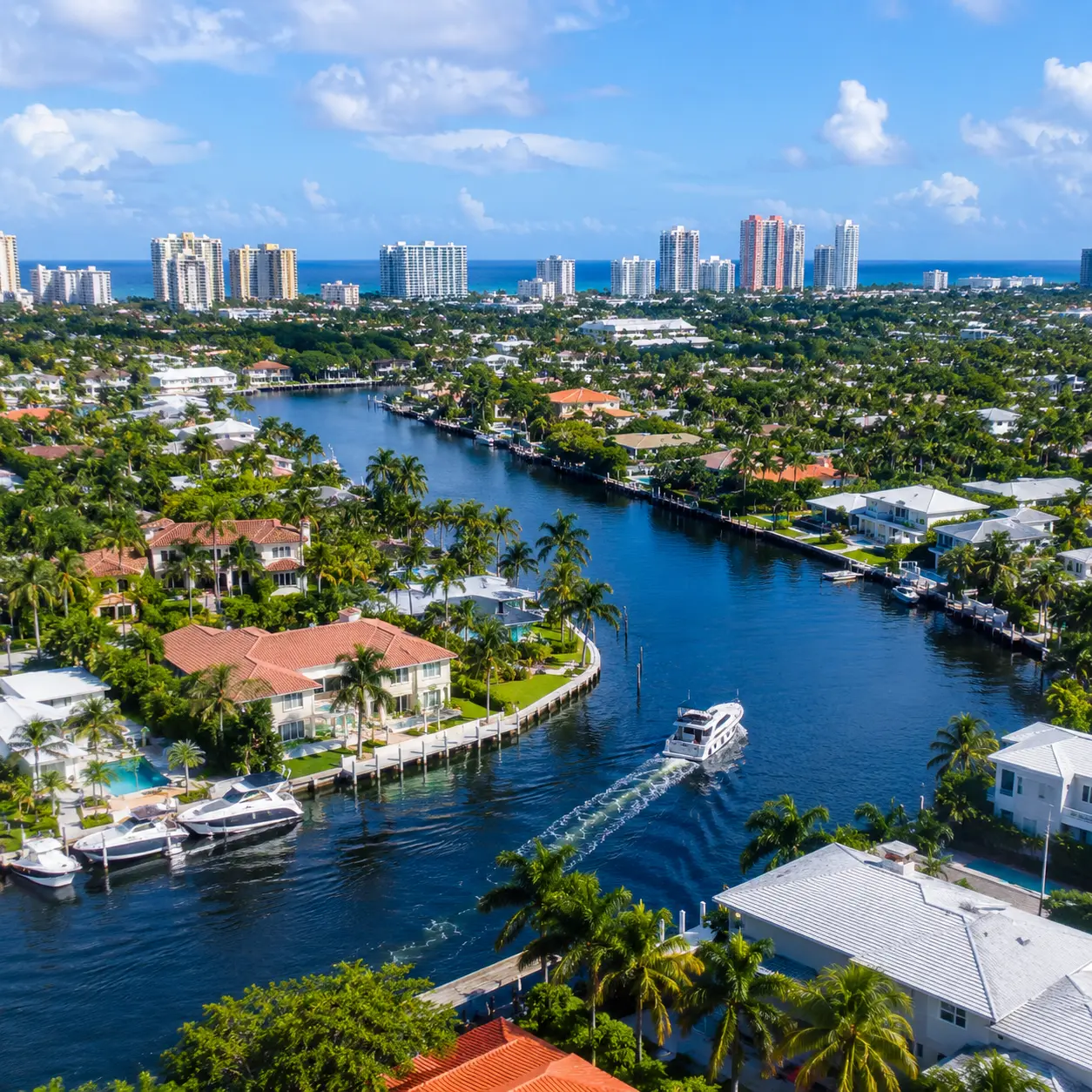 Aerial view of Hollywood Lakes on a sunny day featuring single family homes along the lake with palm trees and sail boats