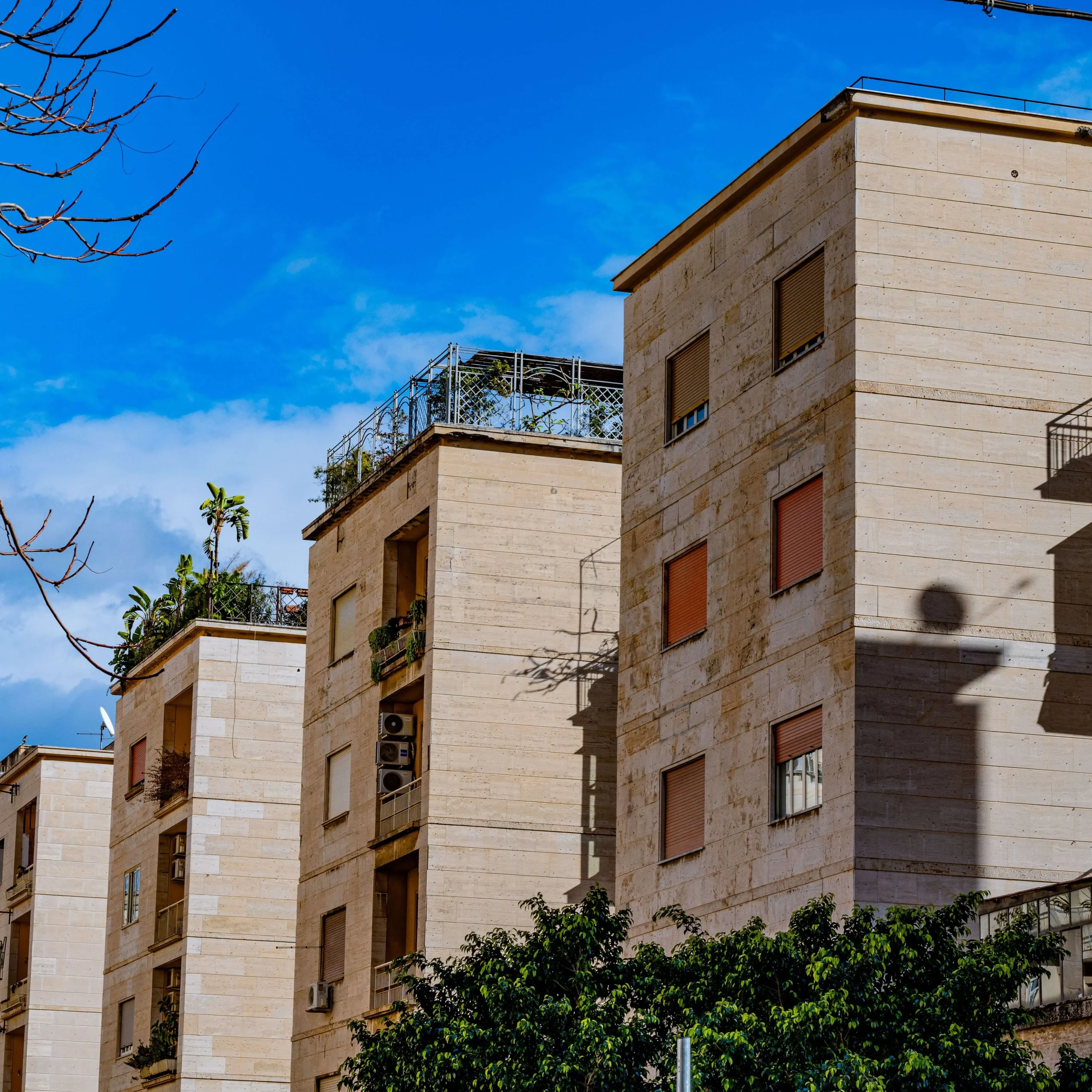 Tan stone apartment buildings with balconies in Spring Tree, Sunrise, FL, viewed from below against a bright blue sky.