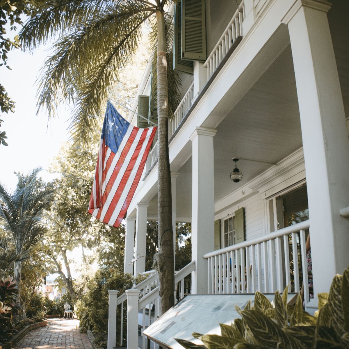 Two-story wooden porch with an American flag and palm tree in Northgate, Lauderdale Lakes